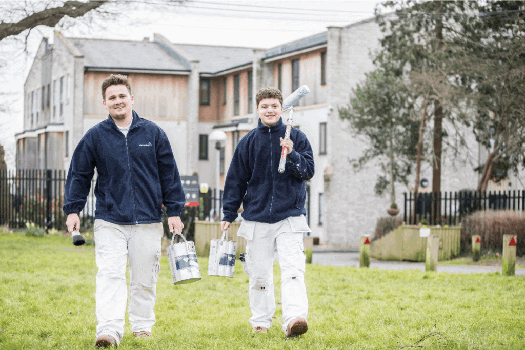 two painters and decorators smiling walking towards camera across a lawn.